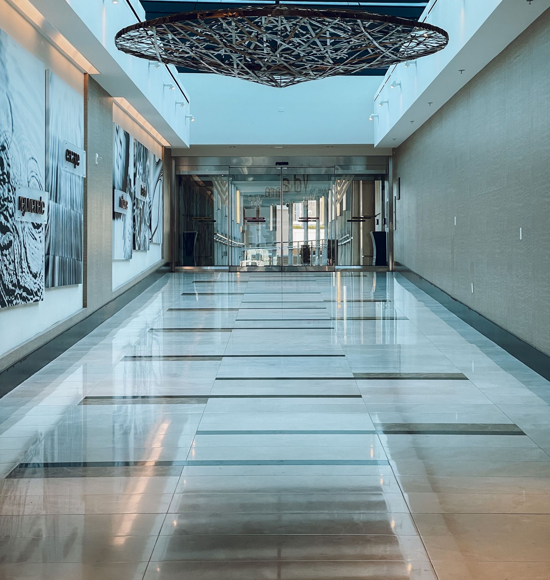 Spacious indoor corridor with polished floors, glass doors, and artistic wall decor.