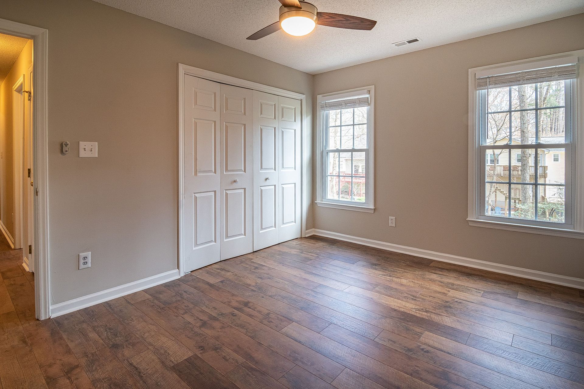 Spacious empty room with hardwood floors, ceiling fan, and natural light from windows.